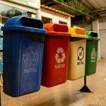 Multiple labeled recycling and waste bins placed together in a clean indoor public area.